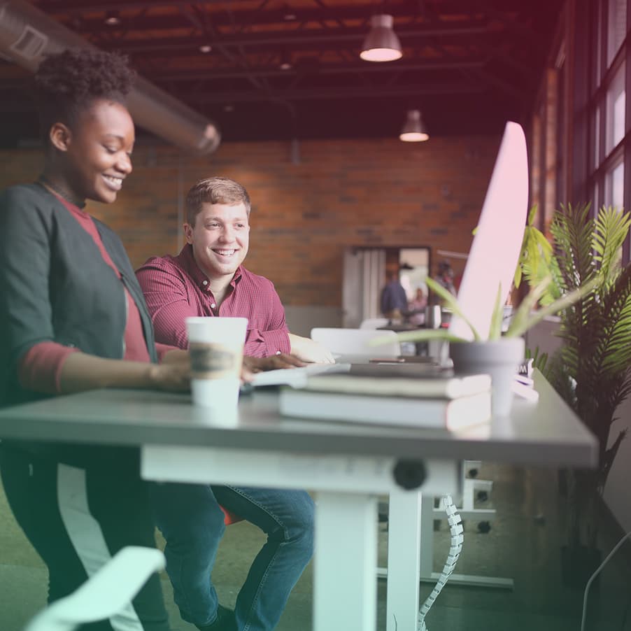 two people working in an office, smiling at a computer monitor